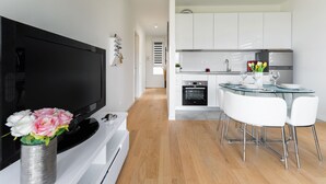 A modern kitchen with white cabinets, a built-in oven, and a dining area with a glass table and white chairs. - StellaMare Apartments (Split)