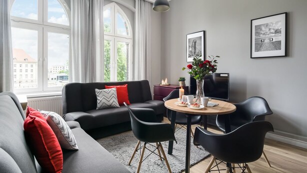 A modern living room with a grey sofa, black chairs, a round wooden table, and a large window with curtains. - Elite Apartments Loft Center (Gdansk)
