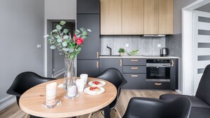 A modern kitchen with dark cabinetry, a wooden dining table, and a vase with flowers. - Elite Apartments Loft Center (Gdansk)