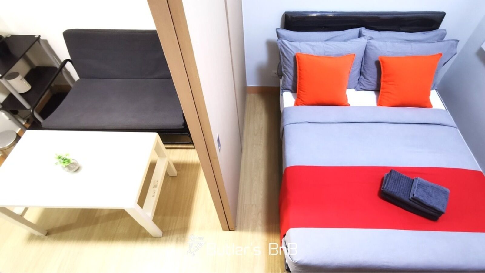 A hotel room with a bed, a small table with a plant, and a bedside table with a book.