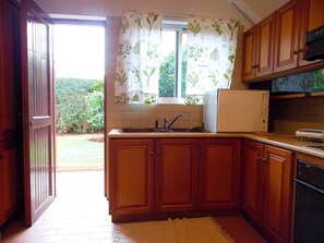 A kitchen with wooden cabinets, a white refrigerator, and a window with floral curtains. - Glyfada Spacious Apartment Garden (Glyfada)