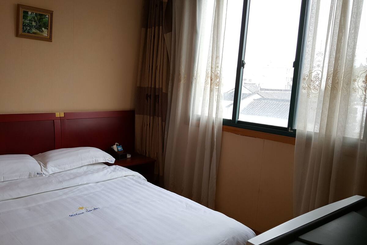 A hotel room with a bed, a nightstand, a telephone, and a window with curtains.