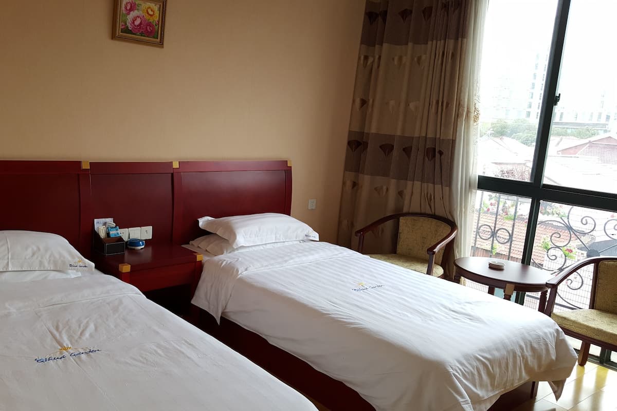 A hotel room with two beds, a small table, a chair, and a window with a view of buildings.