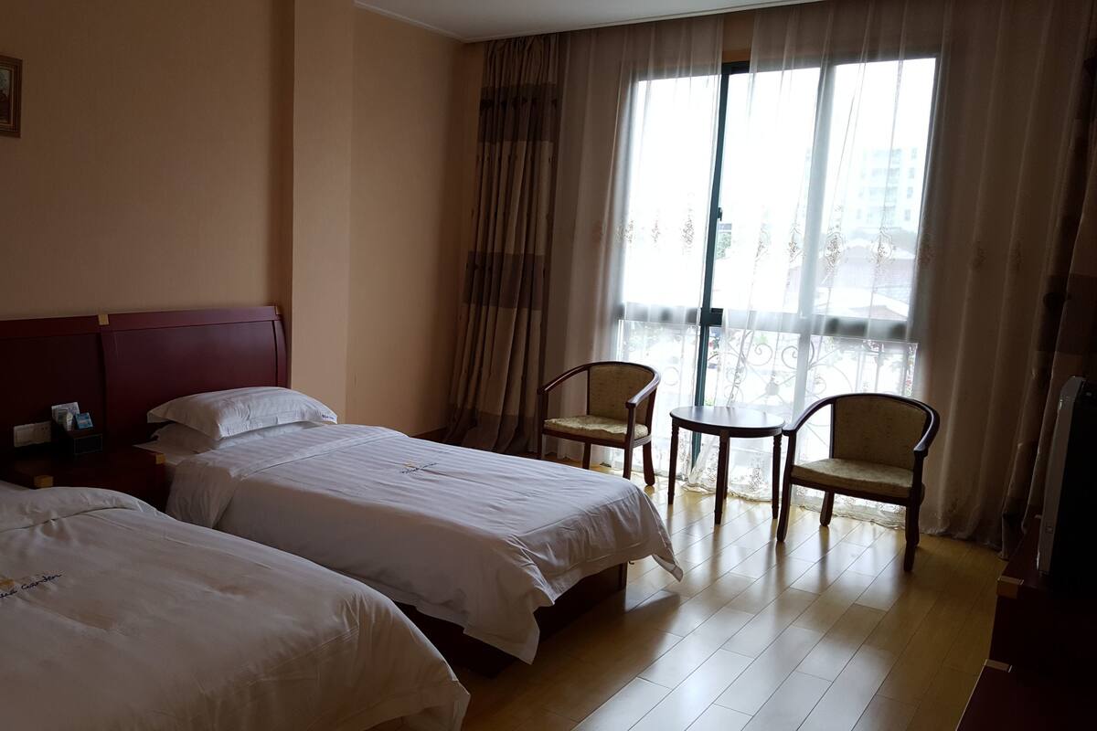 A hotel room with two beds, a nightstand, a chair, and a table.
