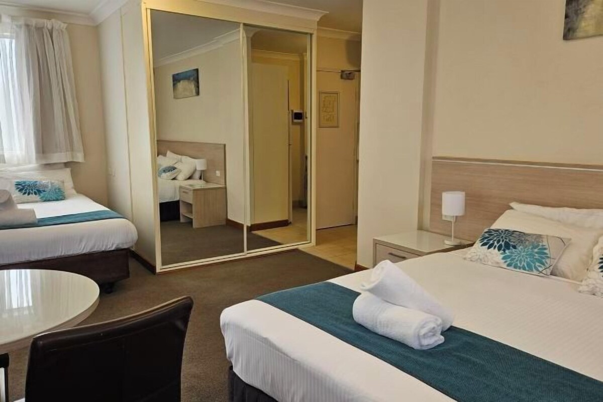 Et hotelværelse med en seng, et spejl, et sengebord, en stol og et rundt bord.