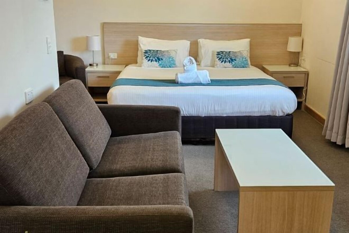 Et hotelværelse med seng, sofa, et natbord og et bord.