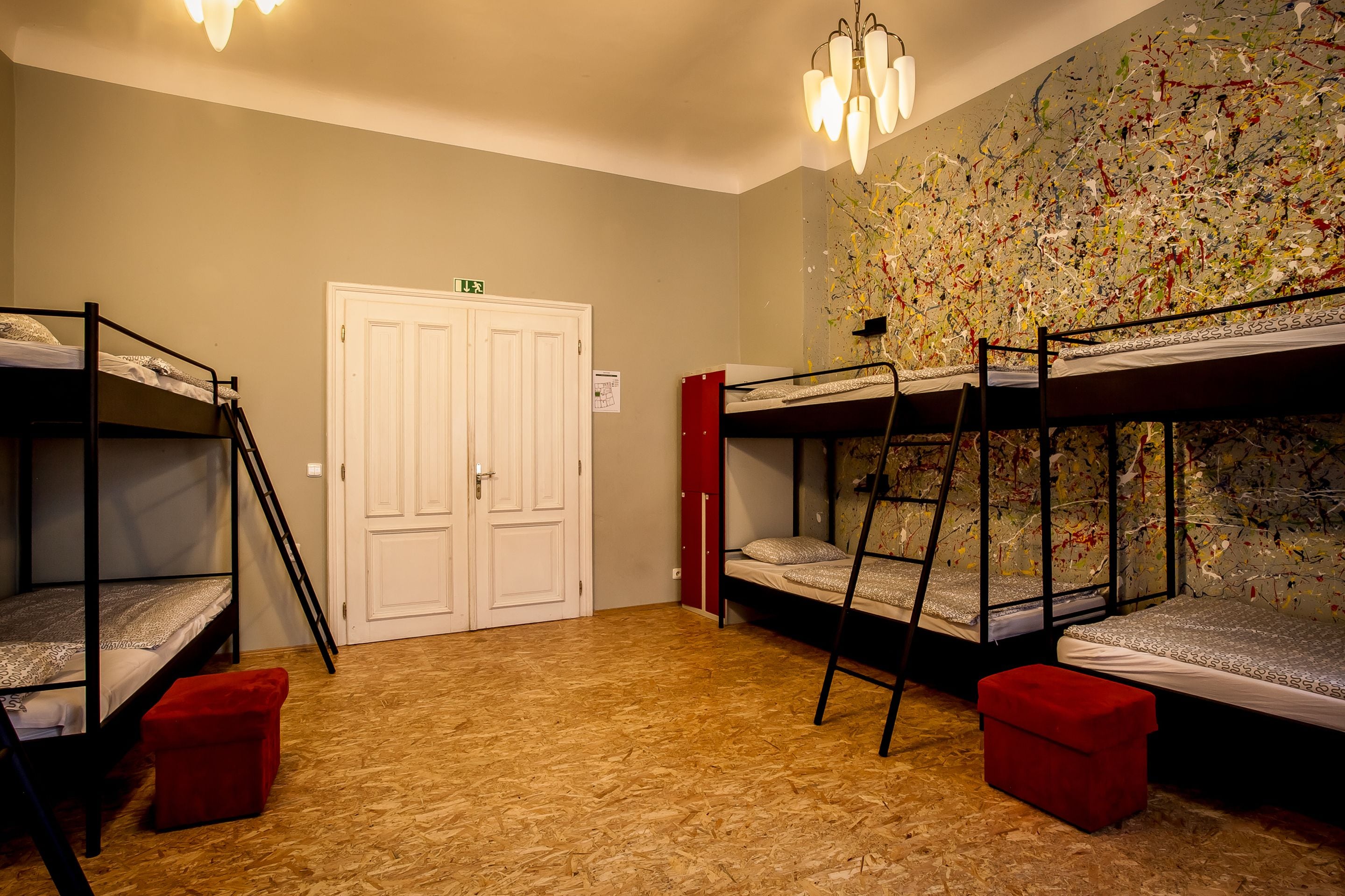 A room with bunk beds, a wooden floor, a white door, and a wall with abstract art.