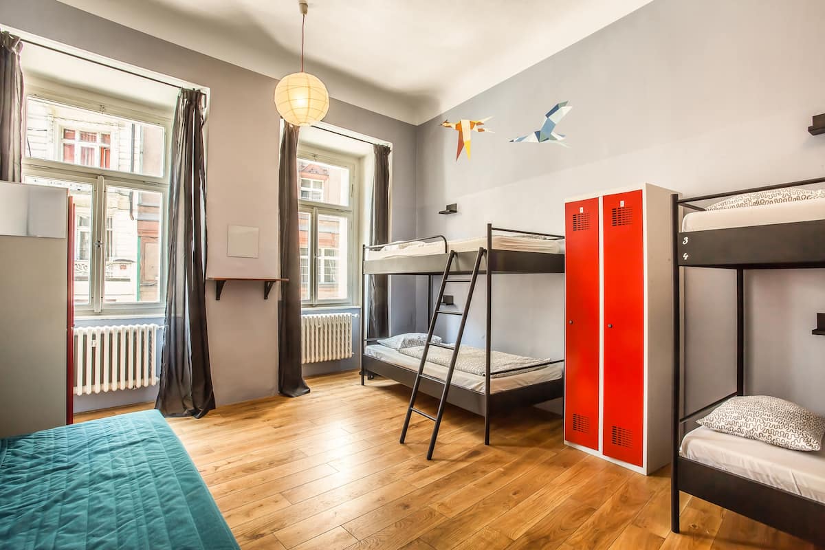 A dormitory room with bunk beds, a window with curtains, a radiator, and a hanging light fixture.