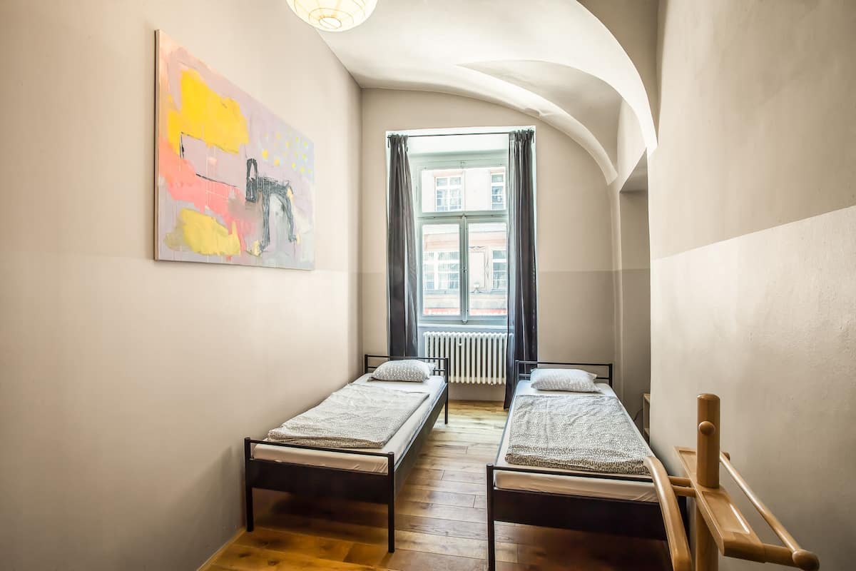 A narrow room with two single beds, a radiator, and a window with curtains.