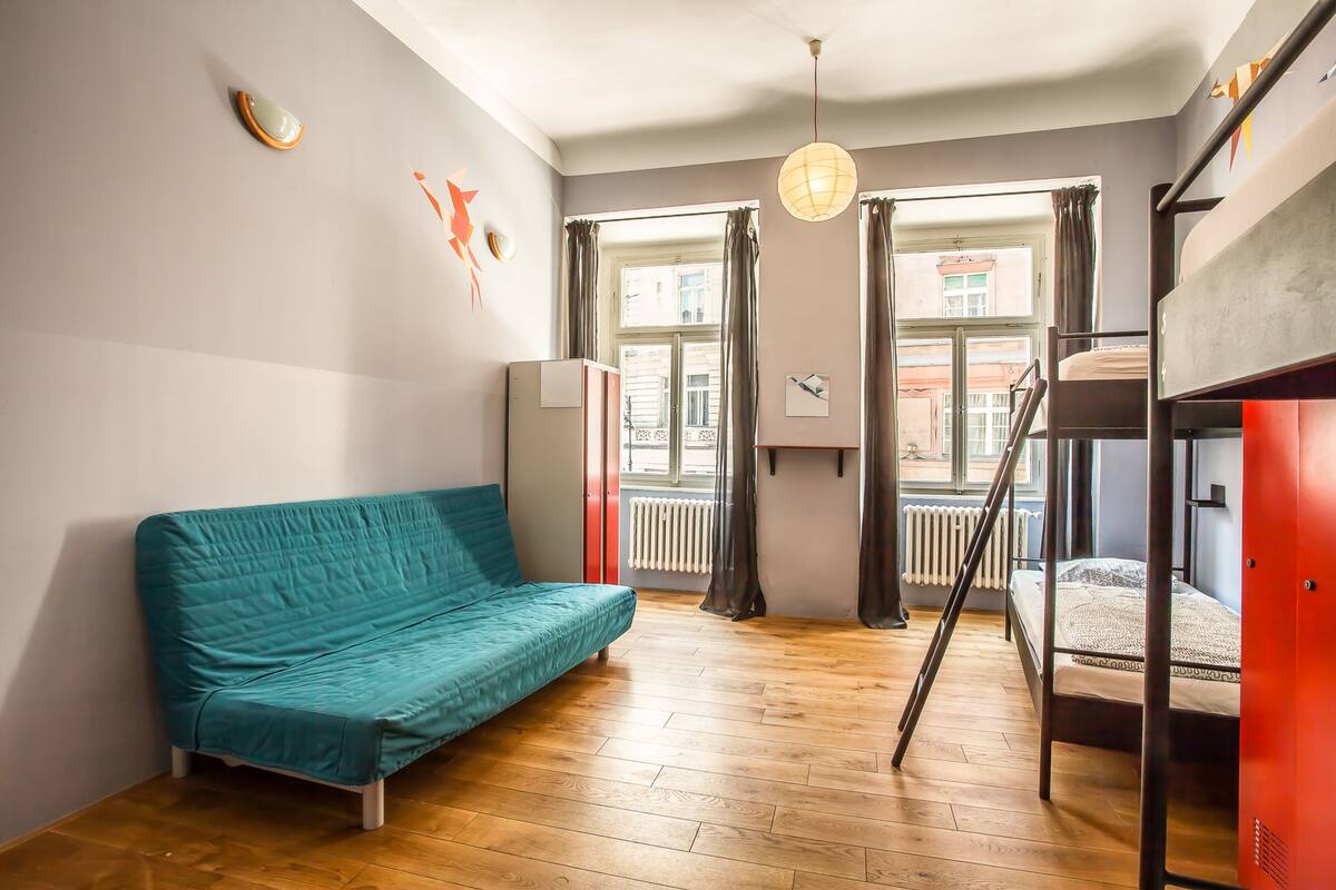 A room with a teal sofa, a bunk bed, a radiator, and a window with curtains.