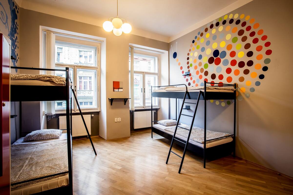 A room with two bunk beds, a wooden floor, a radiator, and a window with a view of buildings.