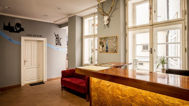 A reception area with a wooden counter, a red sofa, a door, and a wall-mounted deer skull. - Ahoy! Hostel (Prague)