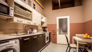 A compact kitchen with a washing machine, microwave, and a dining area with a table and chairs. - Ahoy! Hostel (Prague)