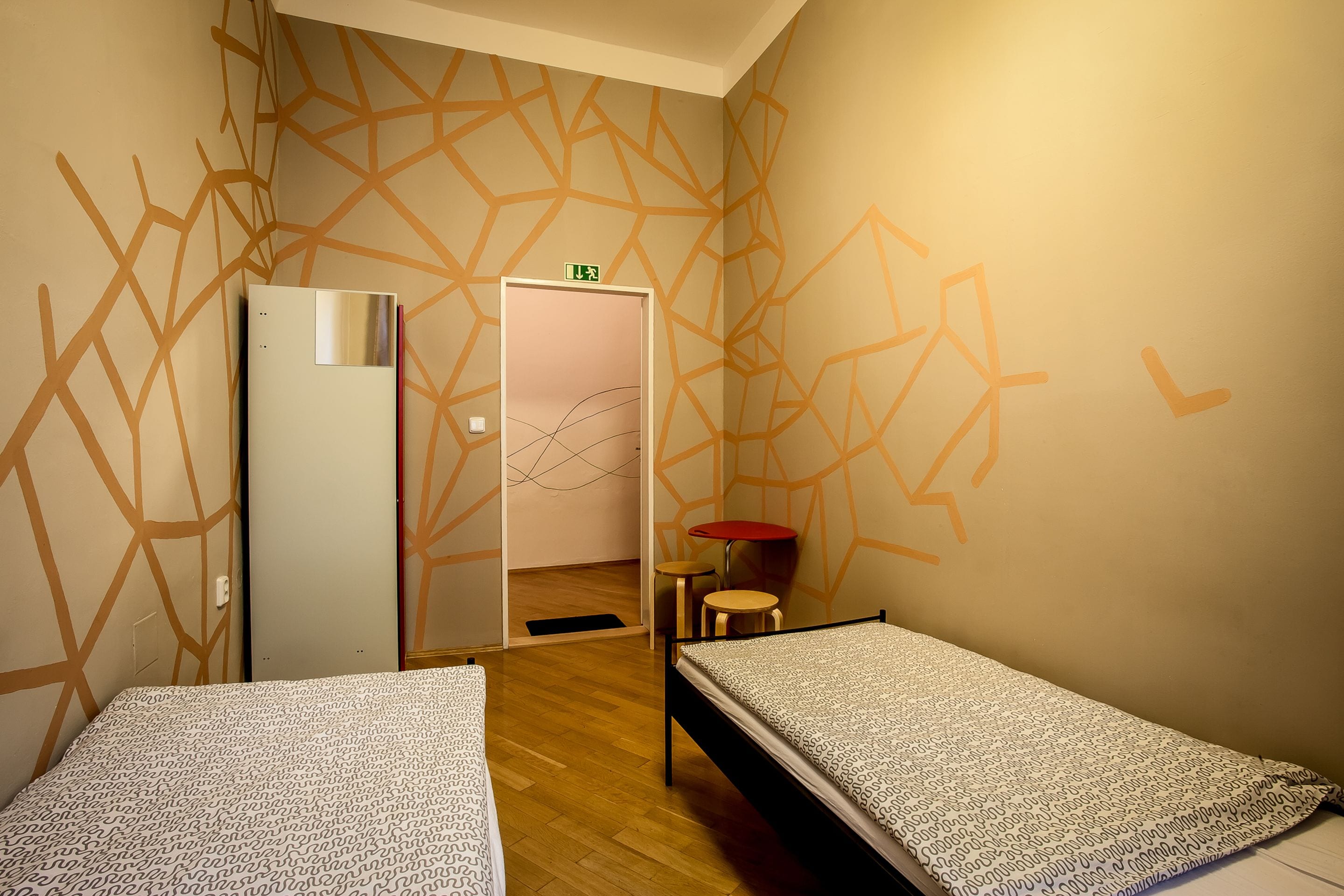 A room with two beds, a small table, and a refrigerator.