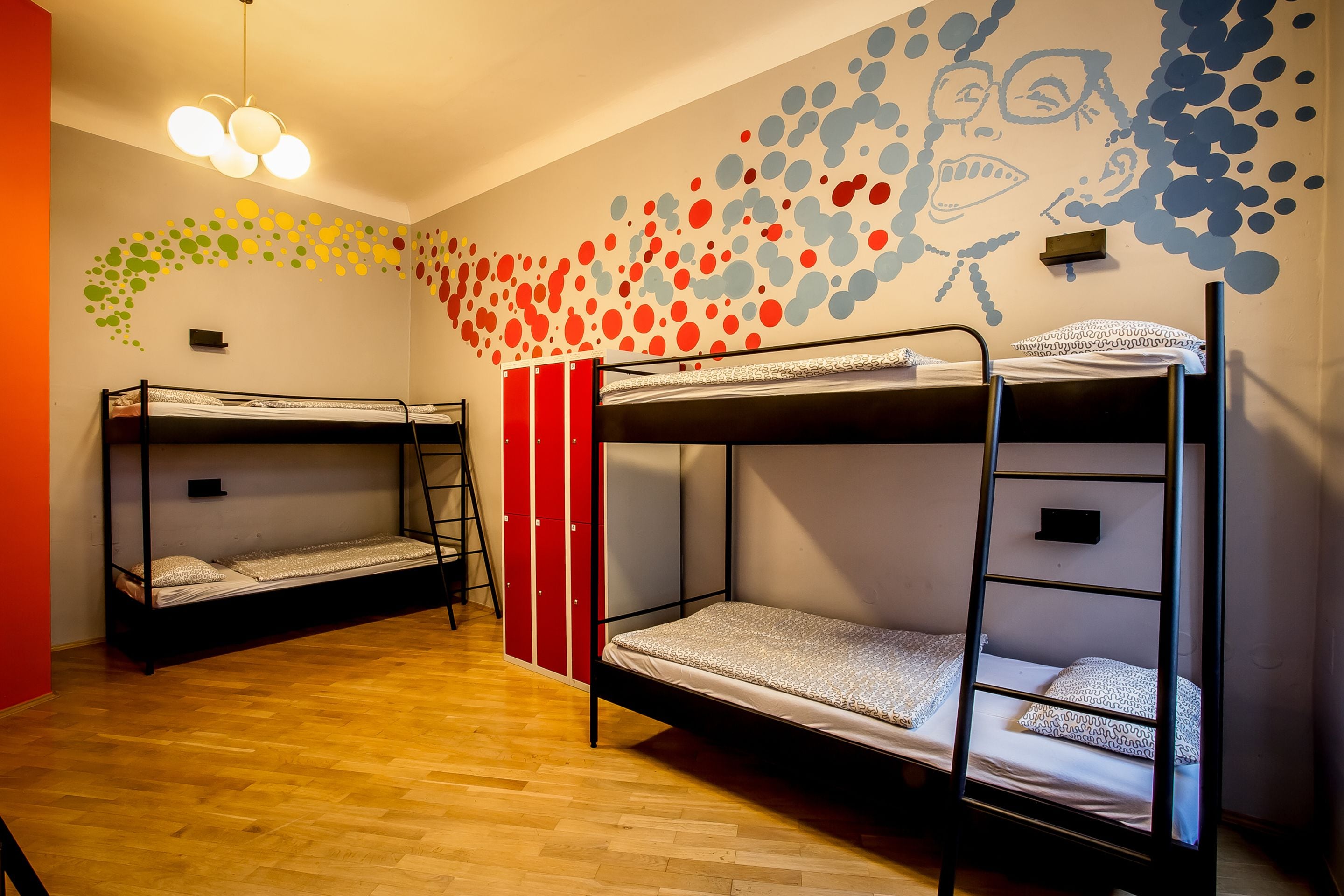 A dormitory room with bunk beds, a wooden floor, and a wall mural.
