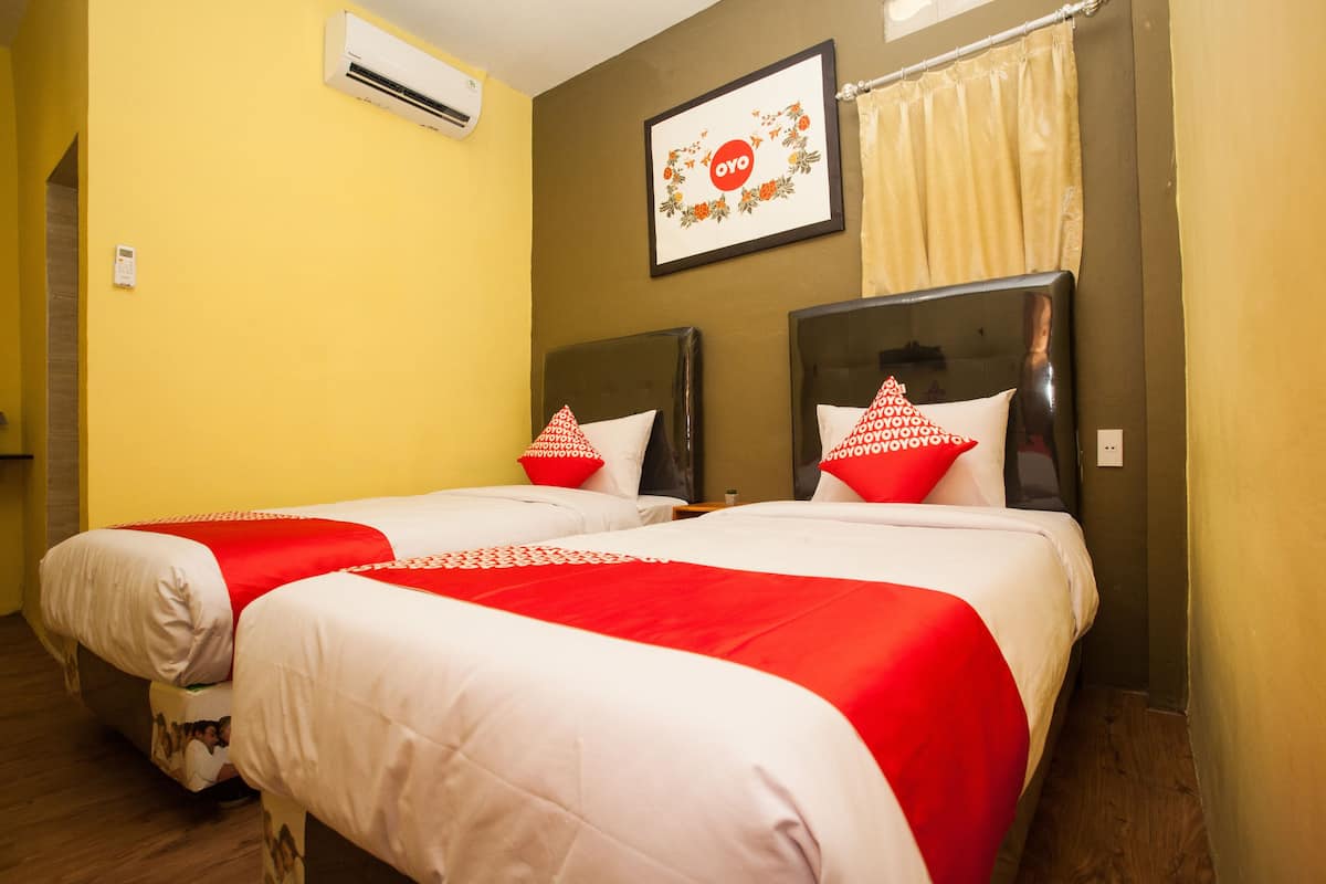 A hotel room with two beds, each with red and white bedding, a framed picture on the wall, and an air conditioning unit.