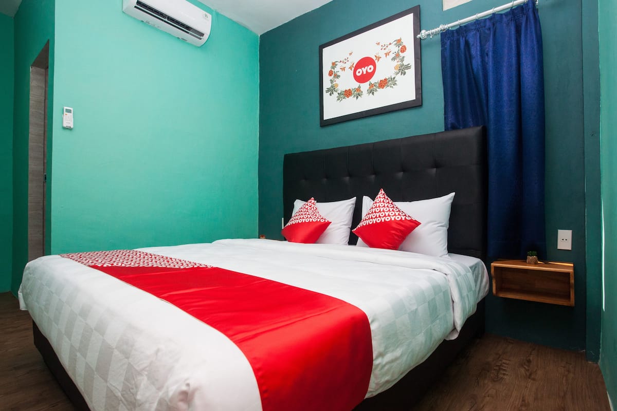A bedroom with teal walls, a black headboard, and a bed with red and white bedding.