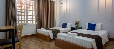 Una habitación de hotel con dos camas individuales, un escritorio de madera, una silla y una ventana con cortinas.