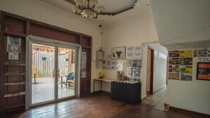 A room with wooden flooring, a glass door leading outside, a small table with cups, and a wall with various posters and notices. - 333 HOSTEL, Siem Reap (Siem Reap)