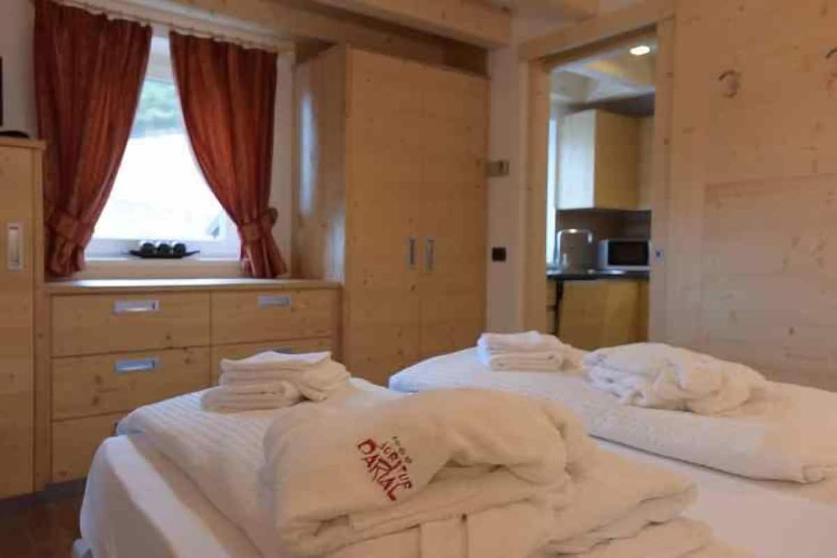 A hotel room with a bed, a window with curtains, a wooden dresser, and a kitchenette area.