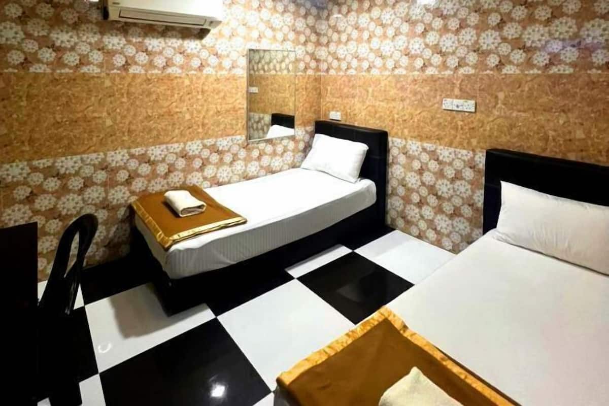Habitación de hotel con dos camas, piso de cuadros, papel tapiz floral y una pequeña mesa con un libro.