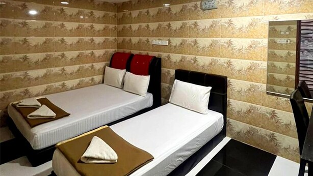 Two single beds with white linens and brown blankets, a black and white tiled floor, and a wall with a floral pattern. - Ark Batu Caves Hotel (Batu Caves)