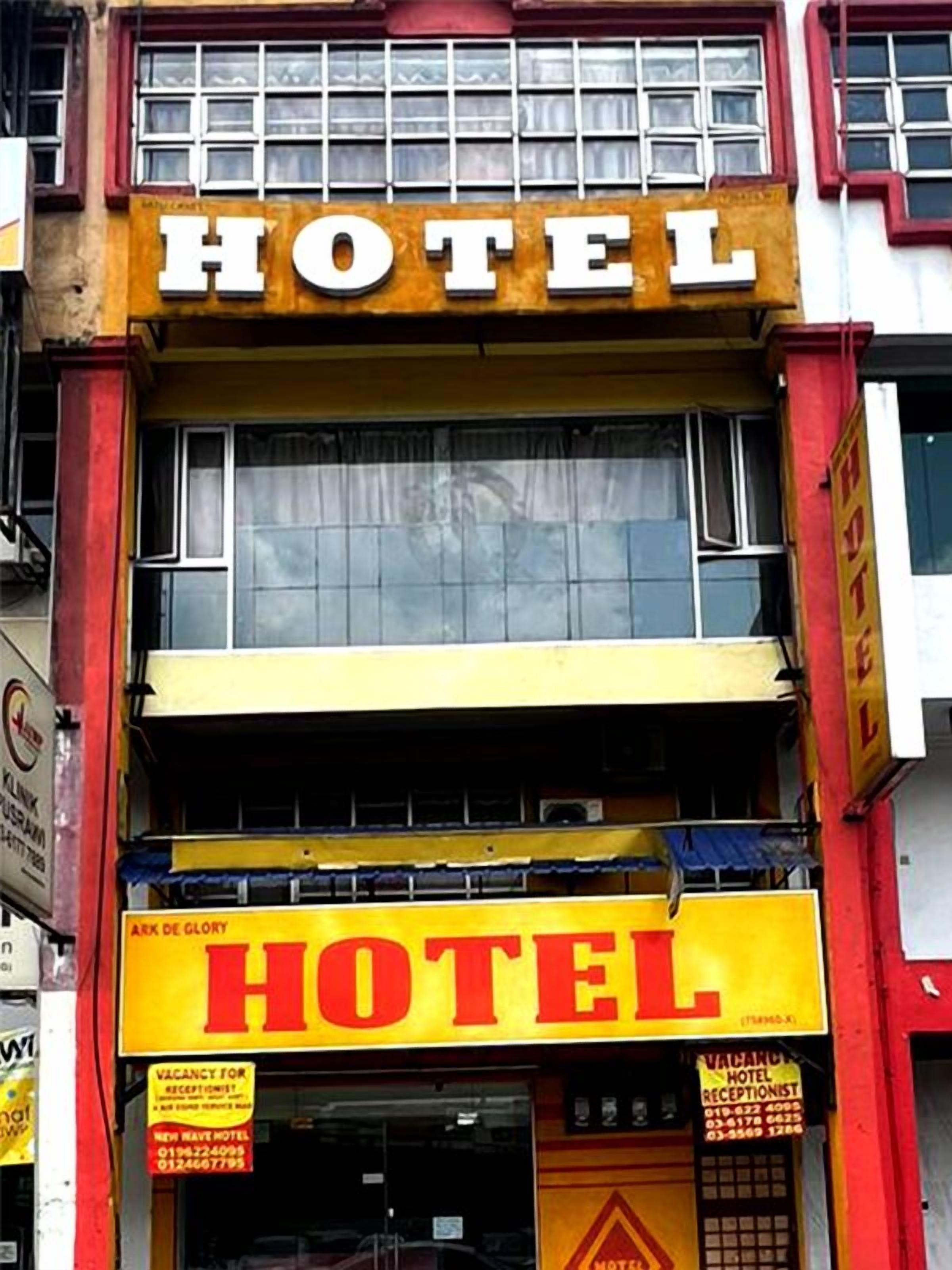 Um hotel com um letreiro grande 'HOTEL' sobre a entrada. Vários sinais indicam vagas para recepcionistas.