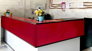 A reception desk with a red and white color scheme, a vase with flowers, and various papers and notices on the wall behind it. - Ark Batu Caves Hotel (Batu Caves)