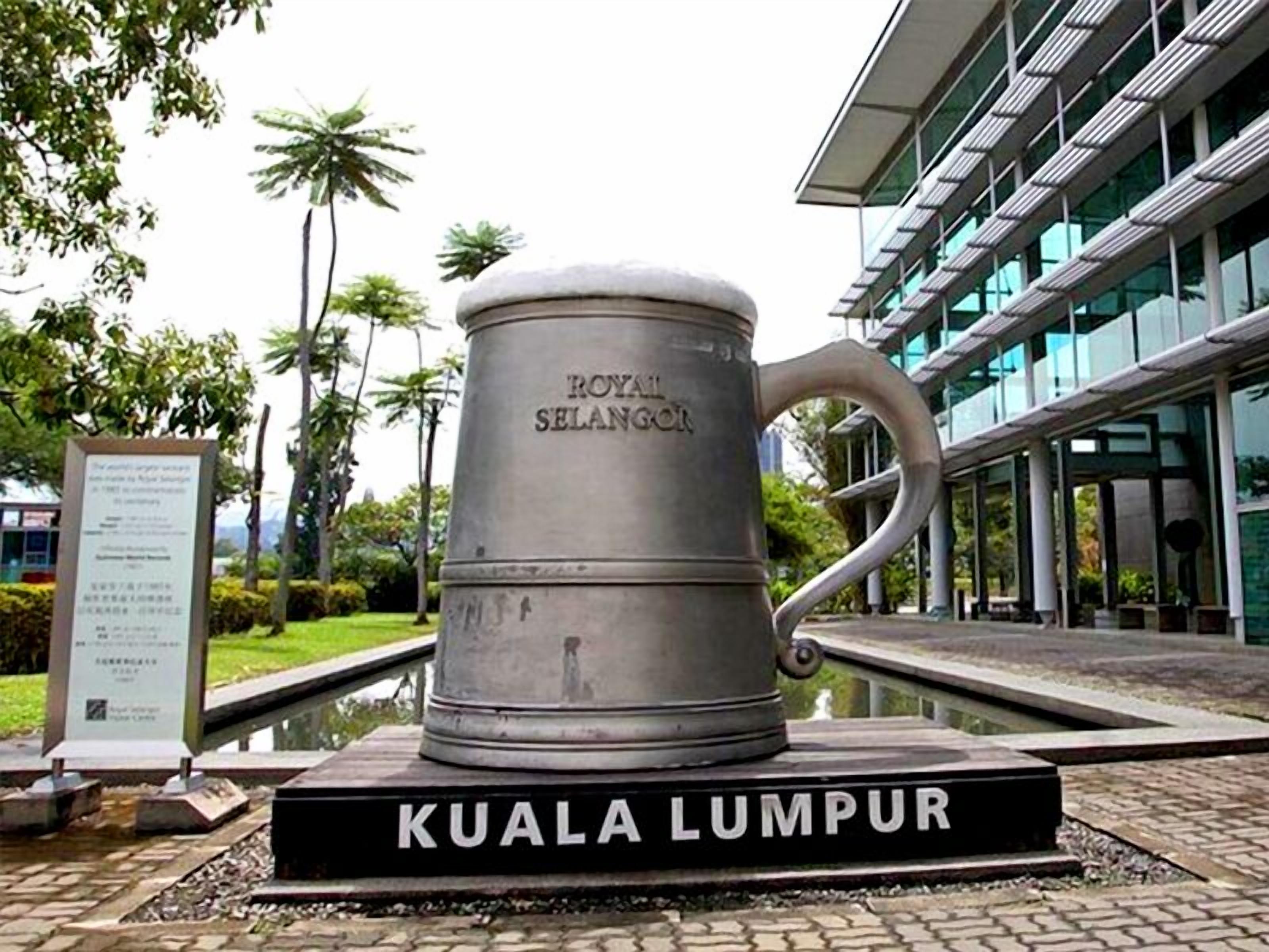 A large metal sculpture of a mug labeled 'Royal Selangor' in front of a modern building with glass windows.