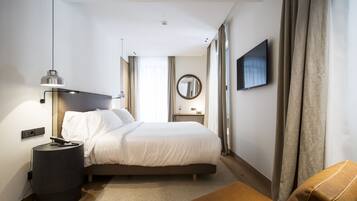 Une chambre d’hôtel moderne avec un grand lit, une table de chevet et un téléviseur à écran plat fixé au mur.