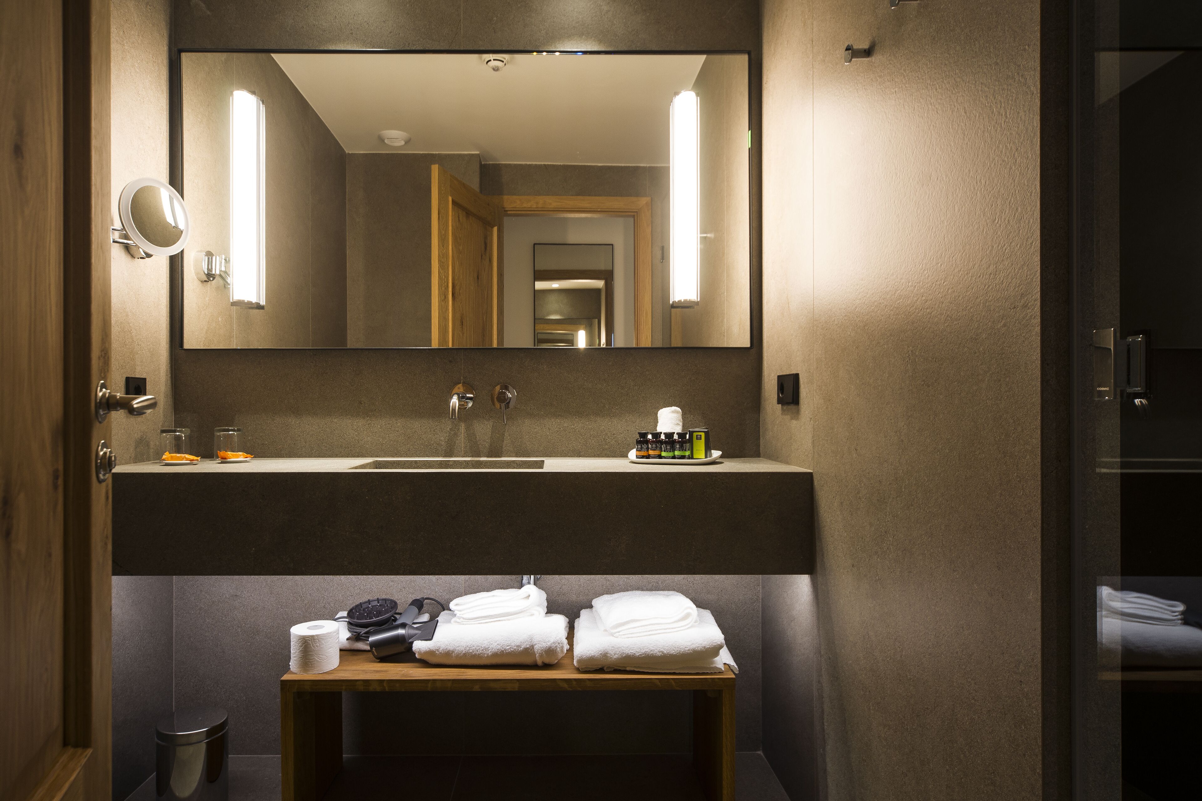 A bathroom with a large mirror, a sink, and a vanity table with towels and toiletries.