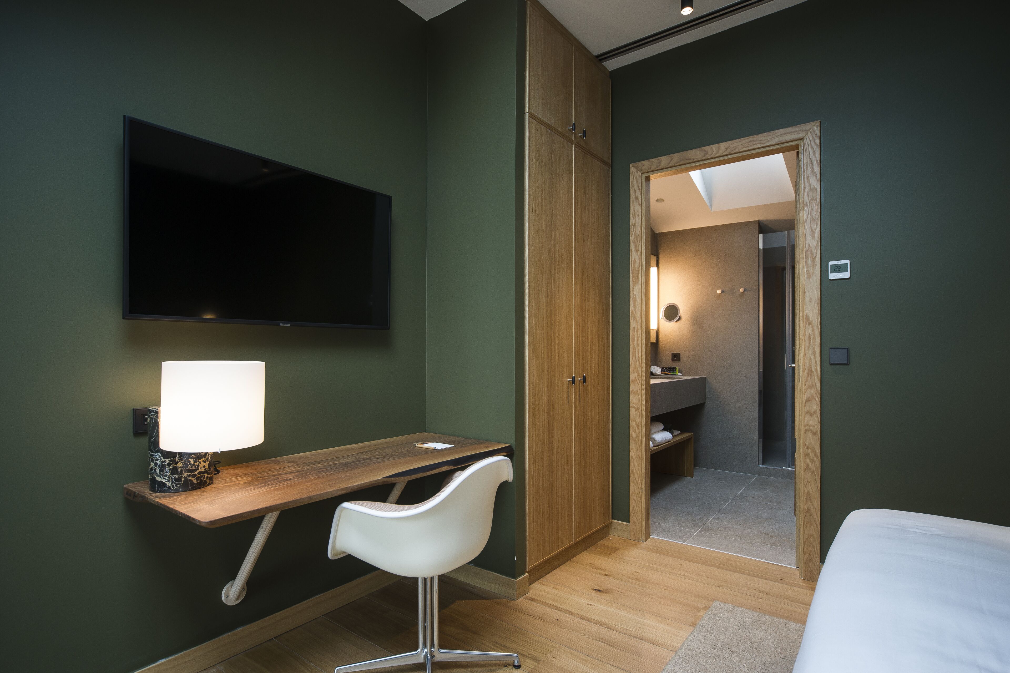 Quarto moderno com escrivaninha de madeira, cadeira branca, TV de tela plana e closet espaçoso.