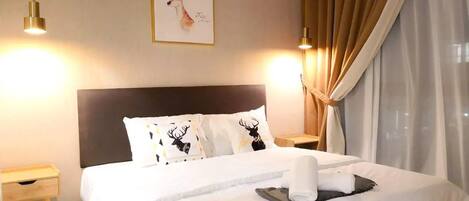 A hotel room with a large bed, two bedside tables, a headboard, a wall-mounted picture, and a window with curtains.