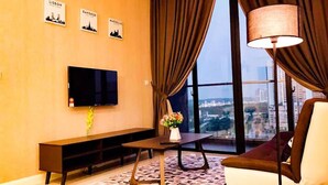 A modern living room with a large window, a flat-screen TV, a sofa, a coffee table, and a lamp. - Legoland D'Pristine Apartment by TGP (Iskandar Puteri)