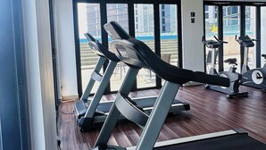 A gym with treadmills and exercise equipment, large windows, and a view of buildings outside. - Legoland D'Pristine Apartment by TGP (Iskandar Puteri)