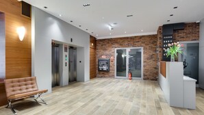 Eine moderne Lobby mit einer braunen Lederbank, zwei Aufzügen, einem Empfangsschalter und einer Ziegelwand.