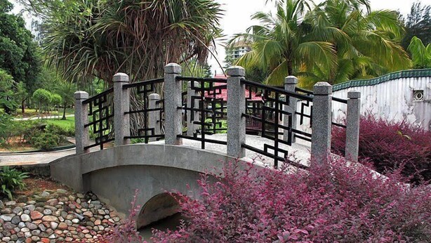A stone bridge with a black metal railing, surrounded by lush greenery and a small stream. - H2 - Sungai Besi Hotel (Seri Kembangan)