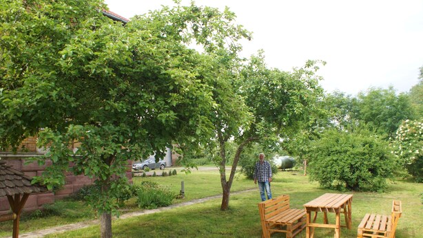 Un jardín con un banco de madera, una mesa y una persona de pie.