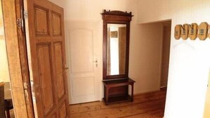 Un pasillo con suelo de madera, una puerta de madera, un espejo y un felpudo.