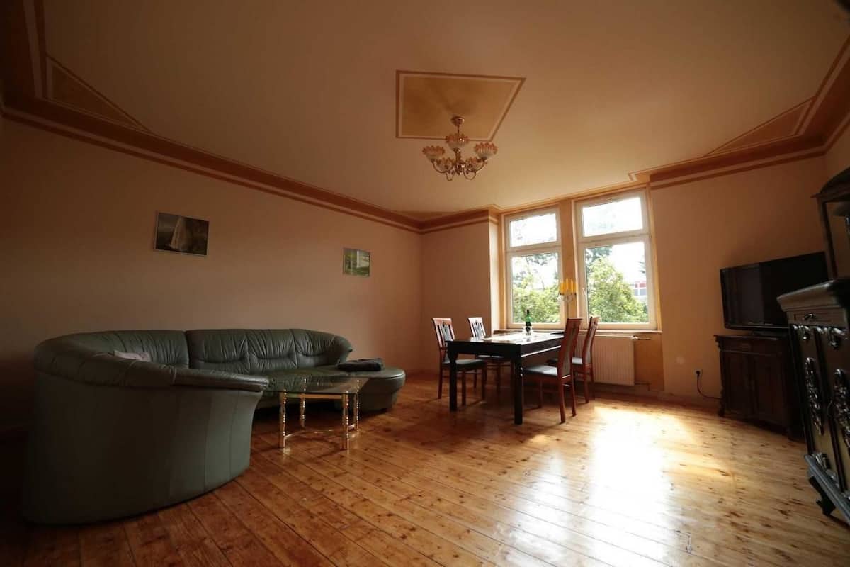 A living room with a curved sofa, a dining table with chairs, a chandelier, and a television.