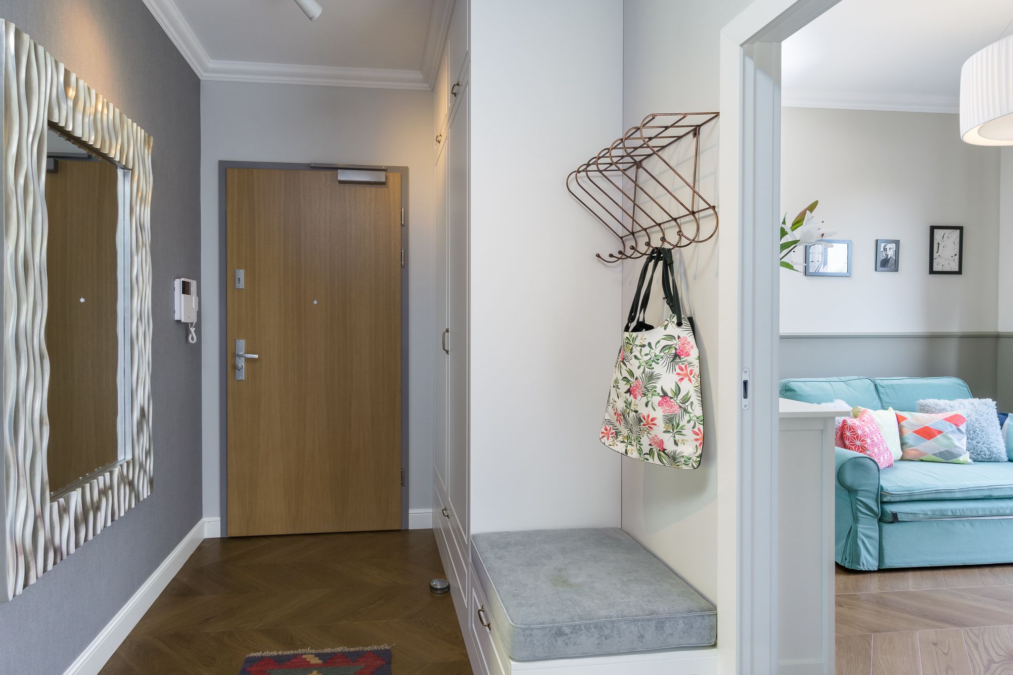 A hallway with a wooden door, a bench, a wall-mounted rack, and a blue sofa with pillows.