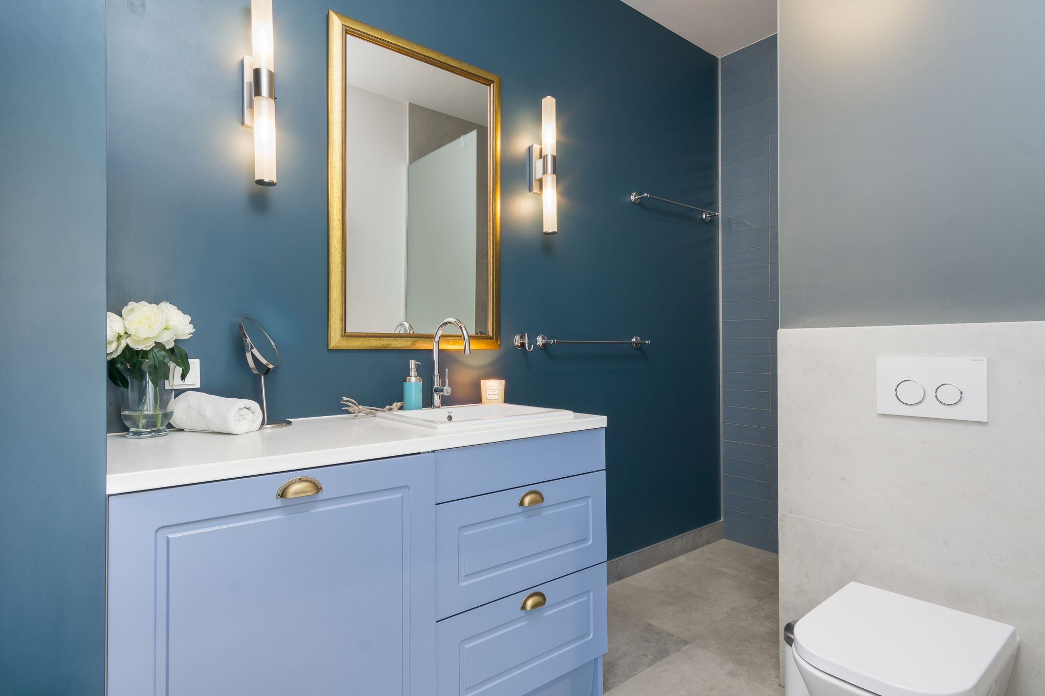 A bathroom with a blue vanity, a white sink, a mirror, and a white toilet.