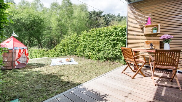 Eine Holzdielen-Terrasse mit Tisch und Stühlen, einem roten Zelt und einer Holzwand mit Regalen.