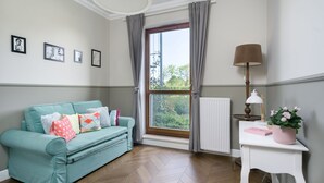 A room with a teal sofa, a white side table with a lamp, and a window with curtains.