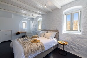 A bedroom with a large bed, a small table, a wardrobe, and a window with a view.