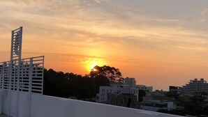 Vista del atardecer desde una azotea con barandilla blanca, edificios al fondo y cielo despejado.