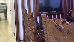 Un salón con un televisor de pantalla plana grande montado en una pared de madera, muebles de madera ornamentados y suelo de baldosas.