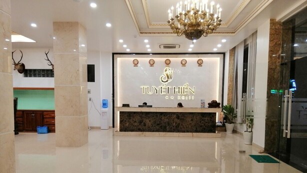 Zona de recepción de un hotel con piso de mármol pulido, un mostrador de recepción y un candelabro.