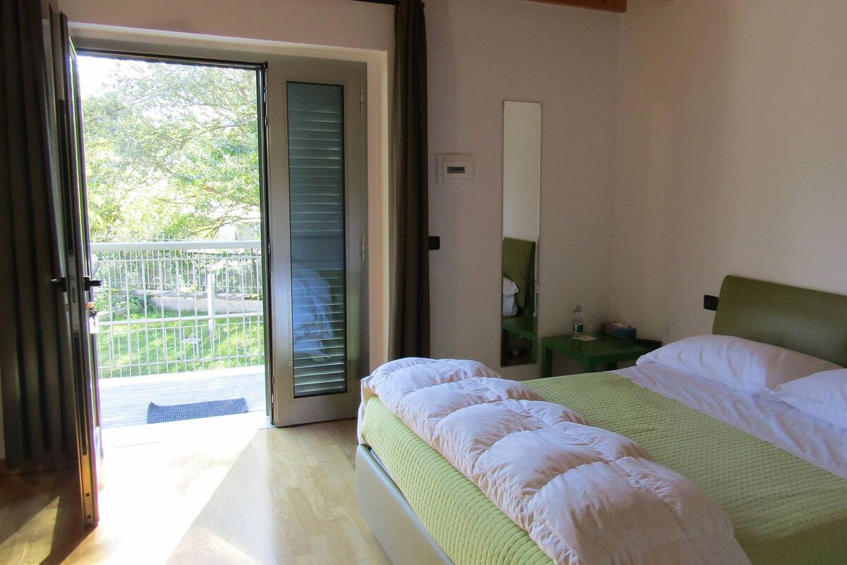 A bedroom with a bed, a nightstand, a mirror, and a sliding glass door leading to a balcony.