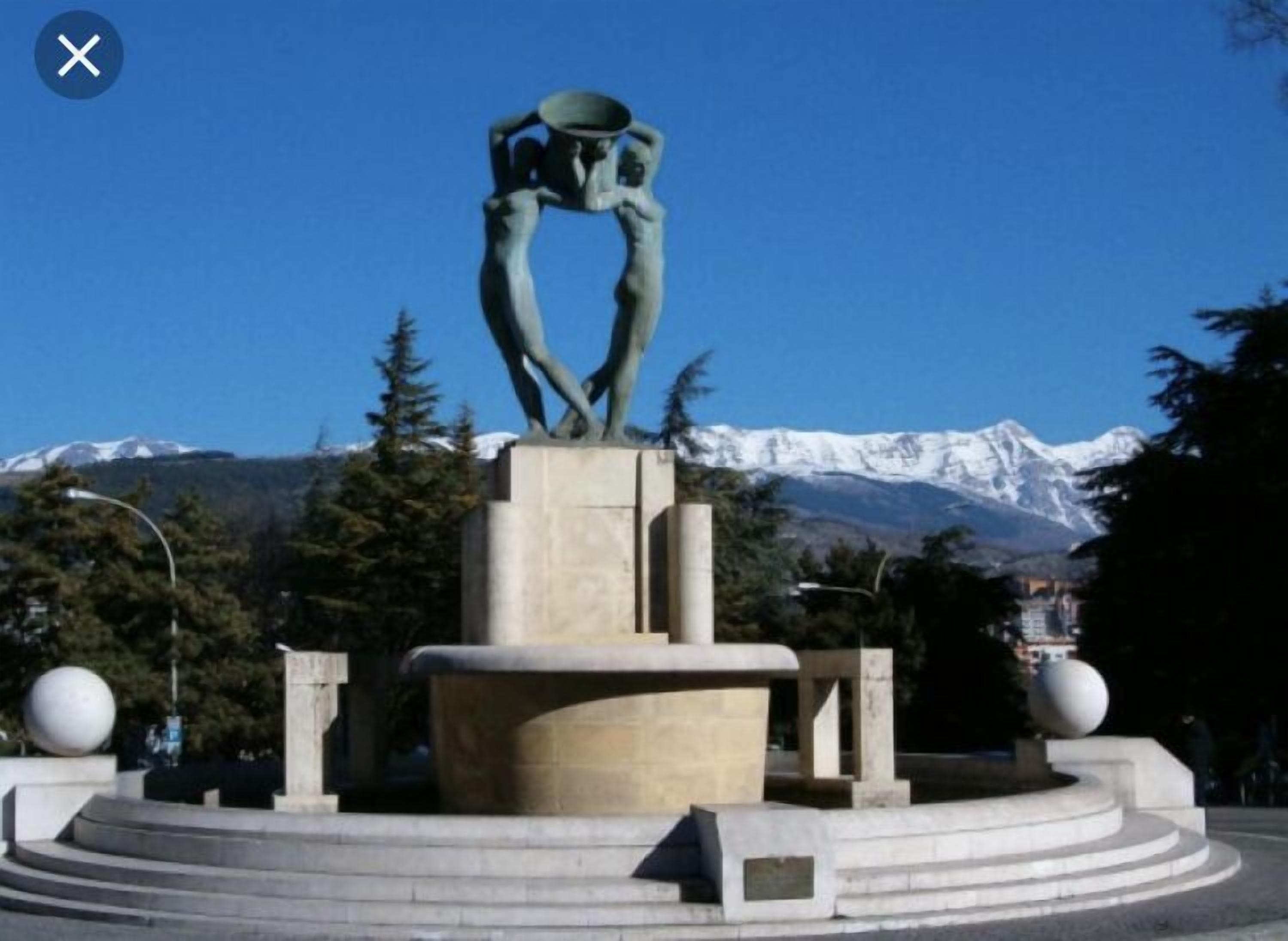 Una escultura en una plaza pública con montañas al fondo.